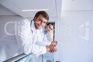 Portrait of smiling doctors leaning on railing in corridor