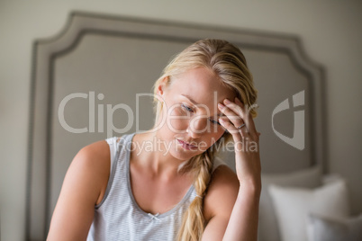 Tense beautiful woman sitting on bed in bedroom