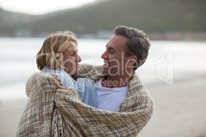 Mature couple wrapped in blanket on the beach