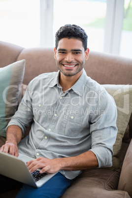 Man sitting on sofa and using laptop in living room at home