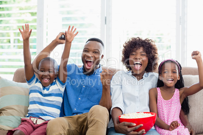 Excited family and kids watching television while having popcorn in living room
