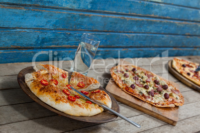 Various italian pizza served with glass of water on wooden plank