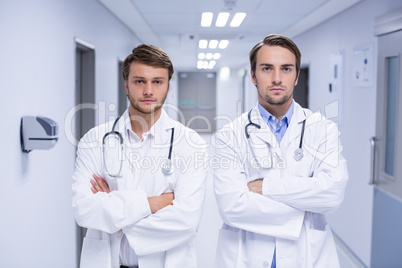 Portrait of doctors standing with arms crossed in corridor