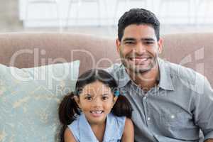Portrait of happy father and daughter sitting on sofa in living room