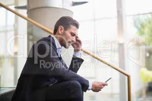 Businessman sitting on steps and using mobile phone