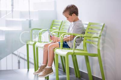 Boy sitting on chair using digital tablet in corridor