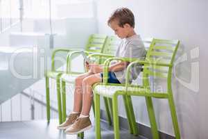 Boy sitting on chair using digital tablet in corridor