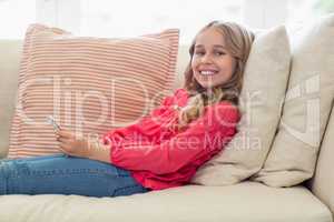 Portrait of smiling girl with mobile phone lying on sofa