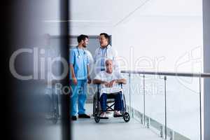 Doctors interacting each other with patient on wheelchair in passageway
