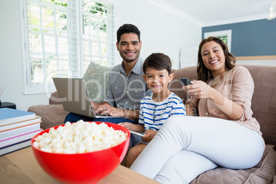 Mother watching television while father and son using laptop and digital tablet at home