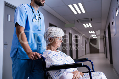 Male doctor pushing senior patient on wheelchair to the ward