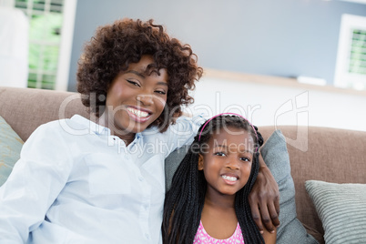 Portrait of mother and daughter sitting on sofa in living room