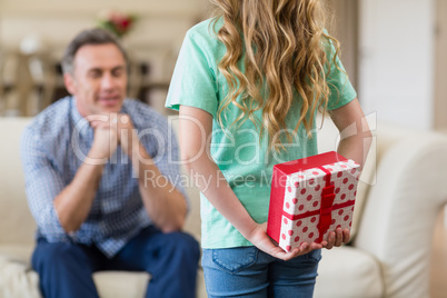 Girl holding surprised gift for her father in living room