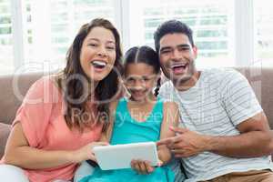 Parents and daughter using digital tablet in living room at home