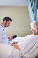 Male doctor discussing medical report over digital tablet with female senior patient in the ward