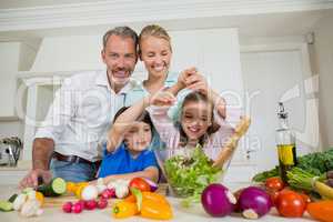Smiling parents and children preparing vegetable salad in kitchen