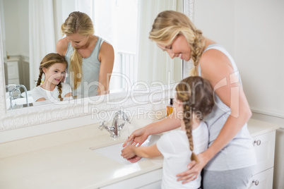 Happy mother and daughter washing hands in bathroom sink