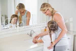 Happy mother and daughter washing hands in bathroom sink
