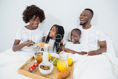 Smiling parents and kids having breakfast in bedroom