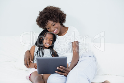 Mother and daughter using digital tablet in bedroom