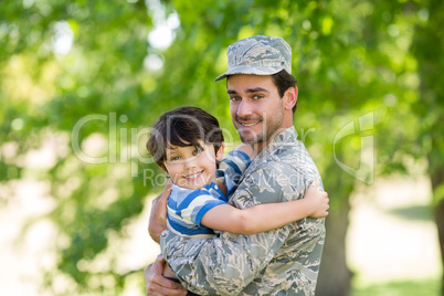 Portrait of army soldier carrying boy in park