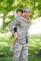Portrait of army soldier giving piggyback ride to boy in park