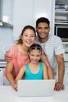 Parents and daughter using laptop in kitchen at home