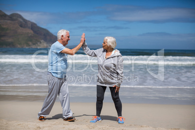 Senior couple giving high five after exercise on the beach