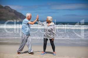 Senior couple giving high five after exercise on the beach