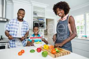 Mother and son preparing salad while father using digital tablet in kitchen at home