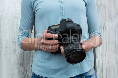 Mid section of female photographer standing against wooden background