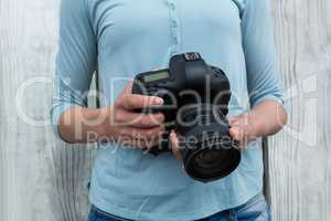 Mid section of female photographer standing against wooden background