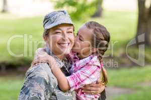 Happy female soldier being kissed by her daughter in park
