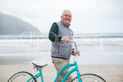 Senior man standing with bicycle on the beach