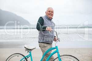 Senior man standing with bicycle on the beach