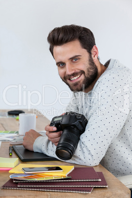 Happy photographer holding camera at his desk