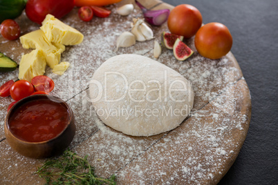 Various ingredients with pizza dough and flour on rolling board