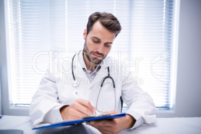 Male doctor writing on clipboard