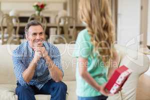Girl holding surprised gift for her father in living room