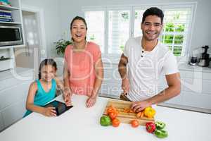 Portrait of daughter and mother using digital tablet while father chopping vegetables in kitchen