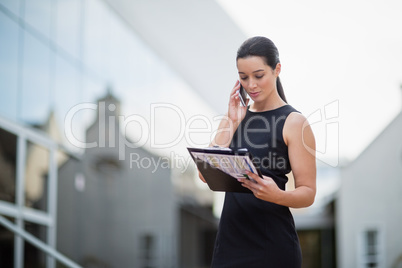 Businesswoman holding clipboard and talking on mobile phone