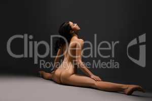 Beautiful naked woman doing splits at dark studio