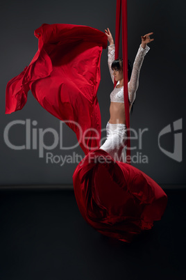 Pretty slim gymnast on red aerial silks in studio