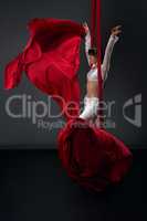 Pretty slim gymnast on red aerial silks in studio