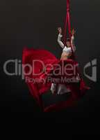 Pretty young gymnast on red aerial silks in studio