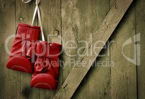 Red leather boxing gloves hang on a nail in the wooden  wall