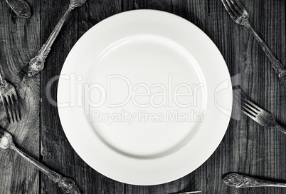 White empty plate among forks, top view