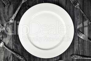 White empty plate among forks, top view