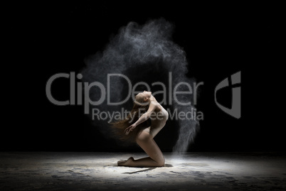 Graceful girl posing in white dust cloud in studio