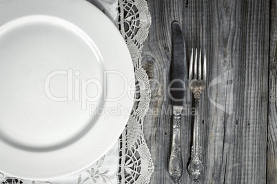 White empty plate on the tablecloth with lace, near knife and fo